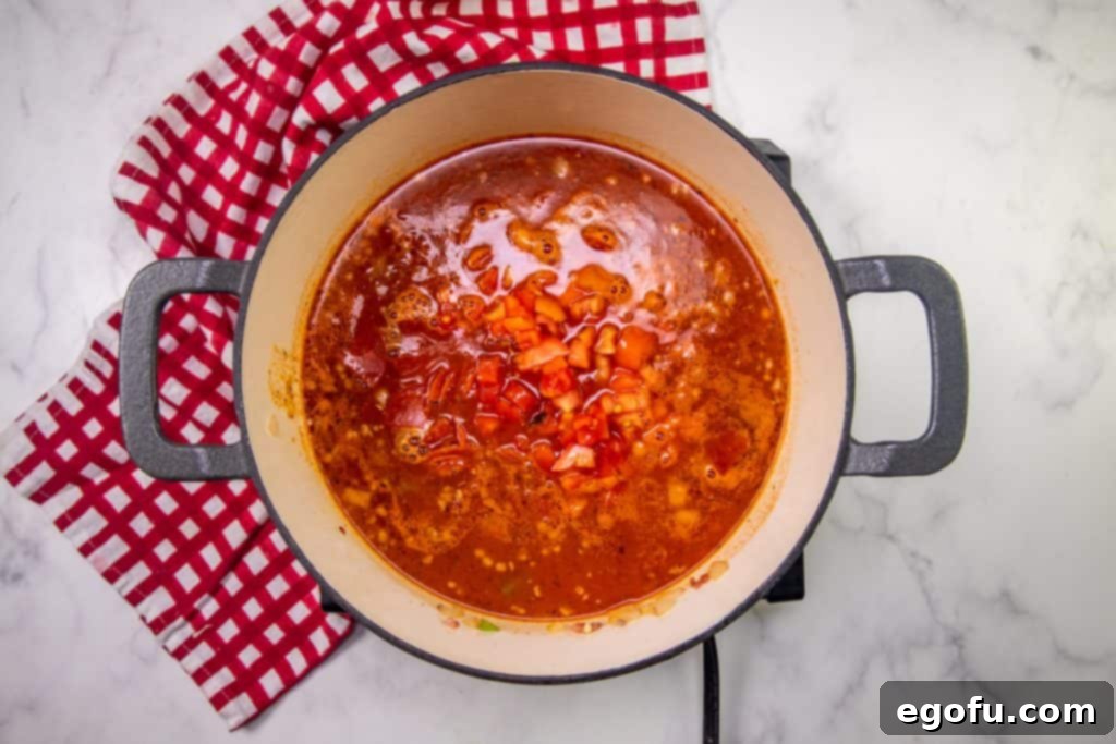 diced tomatoes added to pizza soup in a dutch oven.
