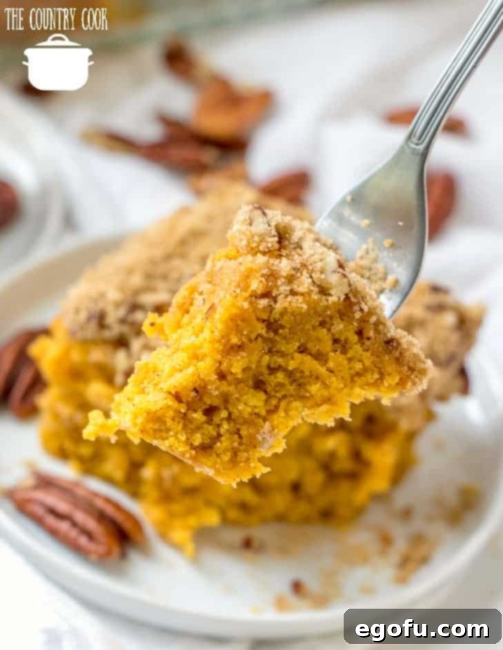 A close-up of a homemade Pumpkin Pie Coffee Cake slice with streusel topping on a white plate, with a fork taking a bite.