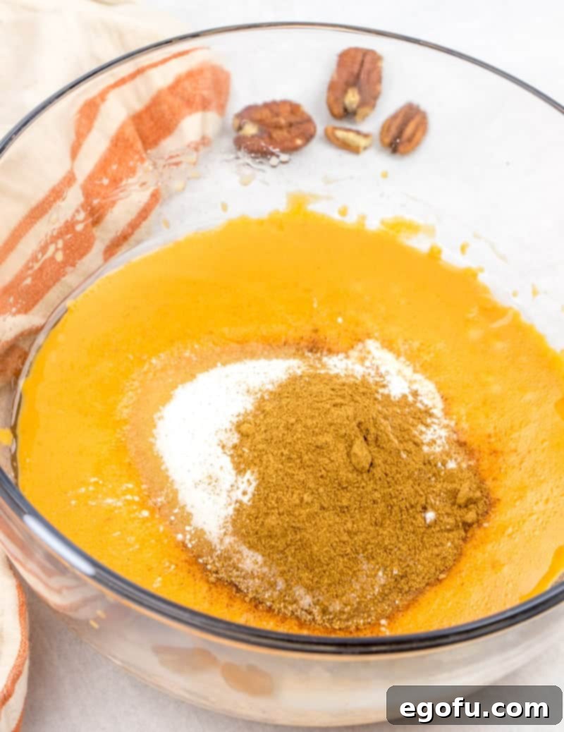 Sugar, baking powder, salt, and pumpkin pie spice being stirred into the pumpkin mixture.