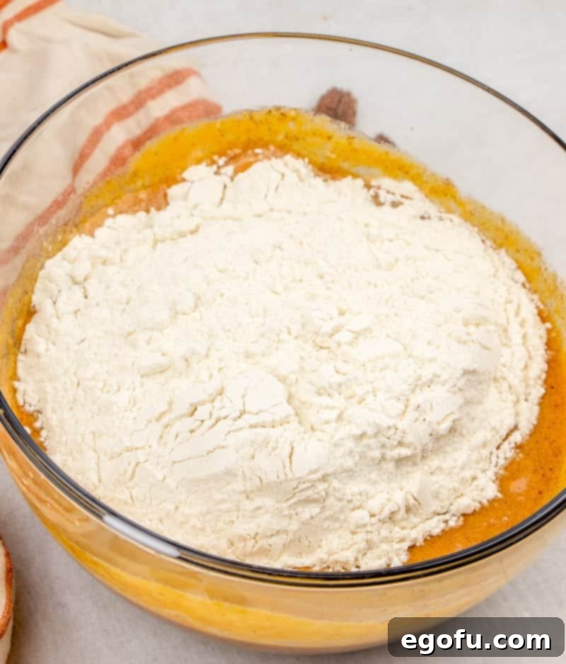 All-purpose flour being gently folded into the pumpkin cake batter.