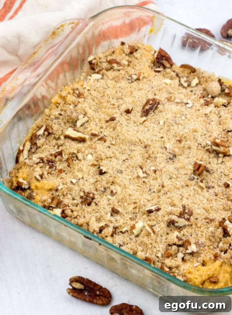 Streusel topping sprinkled over the pumpkin coffee cake batter in a baking dish.