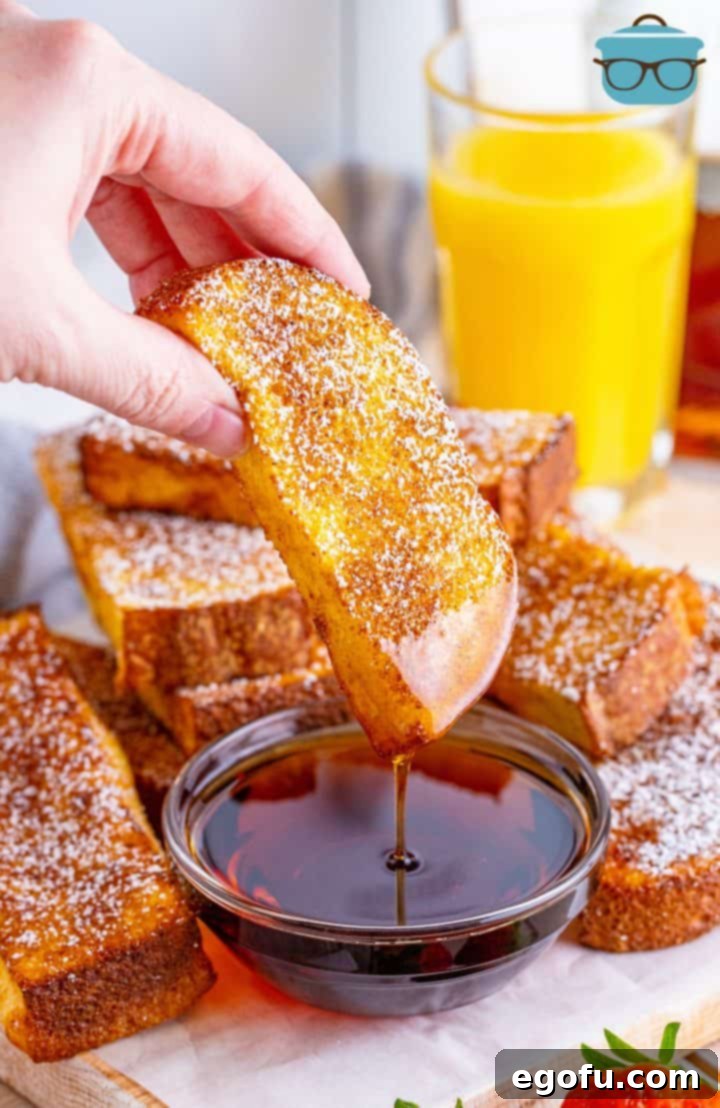 A hand dipping a perfectly golden brown Air Fryer French Toast Stick into a small bowl of rich maple syrup, showcasing its delicious appeal.