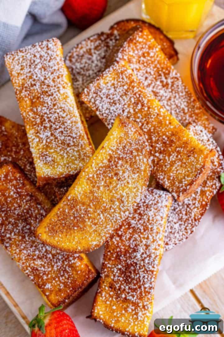 A delightful stack of golden Air Fryer French Toast Sticks presented on a rustic wooden board, accompanied by fresh strawberries and a small bowl of maple syrup, inviting a delicious breakfast.