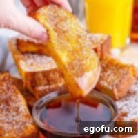 A hand dipping a French toast stick into a small bowl of maple syrup.