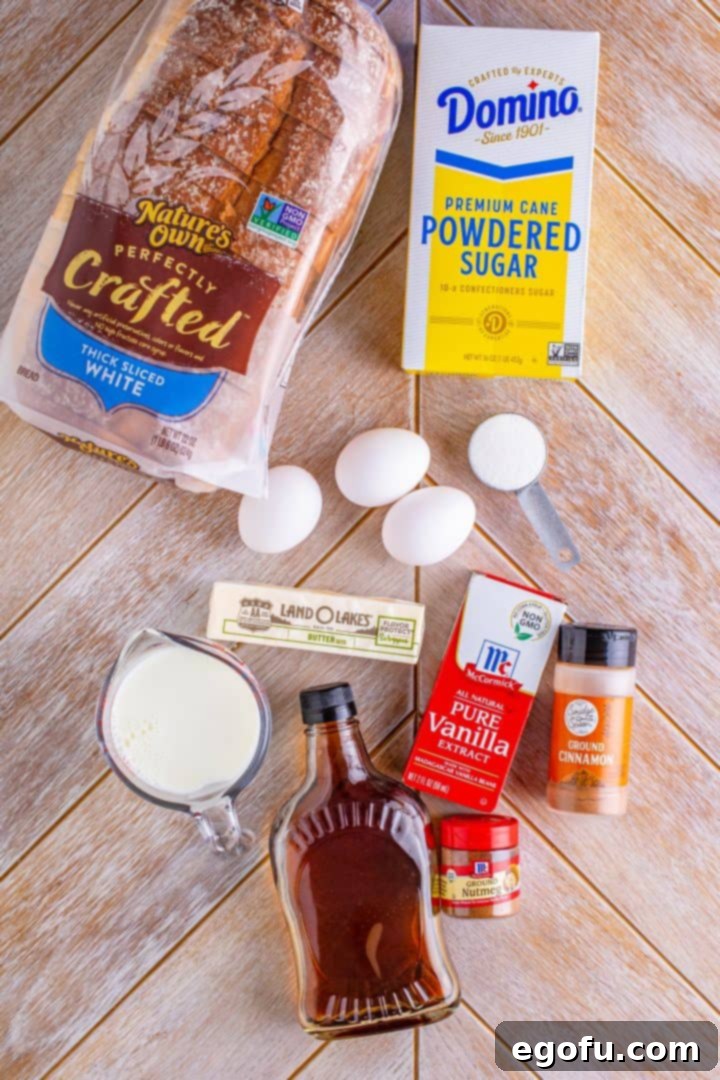 All the fresh ingredients neatly laid out on a clean counter: slices of thick bread, a bowl of milk, fresh eggs, a stick of butter, a bottle of vanilla extract, cinnamon, nutmeg, granulated sugar, a small pitcher of maple syrup, and a shaker of powdered sugar.
