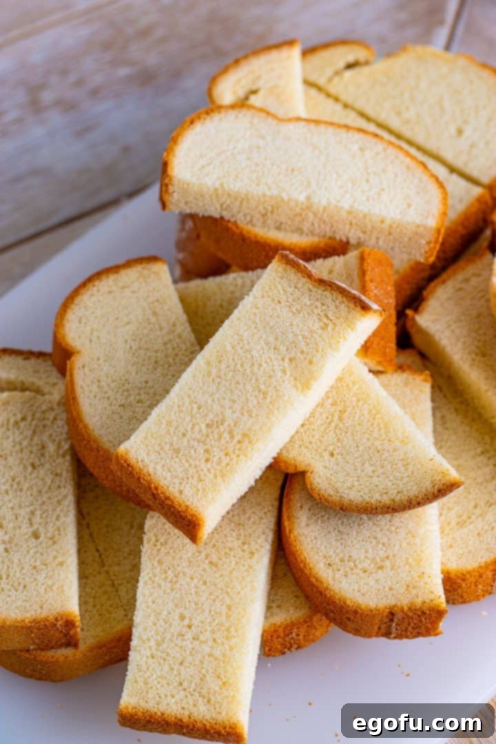 Several slices of thick white bread, expertly cut into thirds and neatly stacked on a white rectangular platter, ready for the next step of preparation.