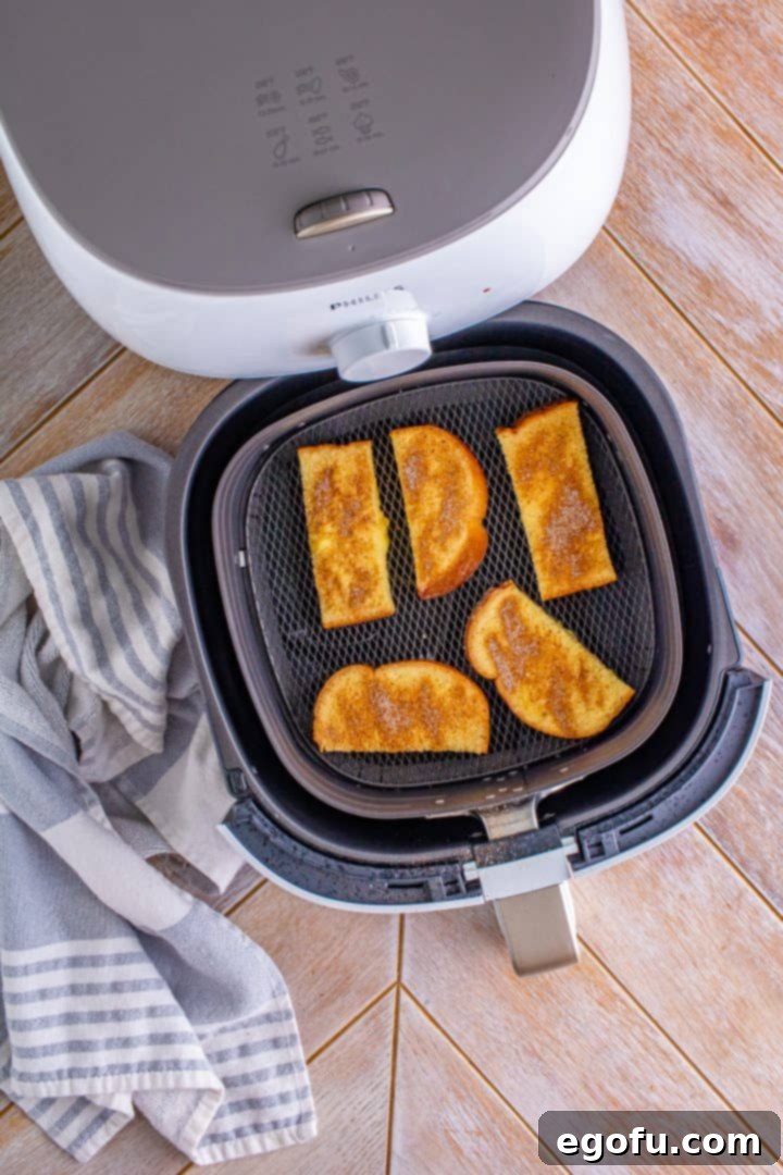 Uncooked, battered French toast slices are neatly arranged in a single layer within the basket of an air fryer, poised for cooking.