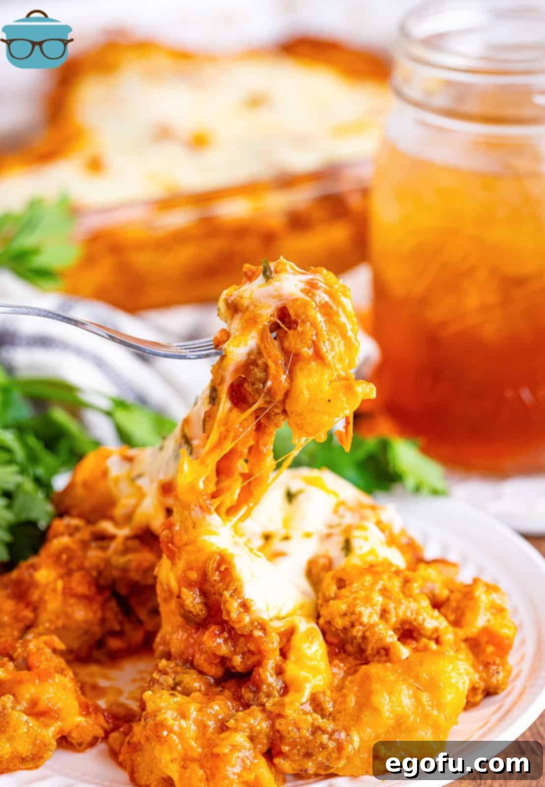 A fork lifts a perfectly cooked, cheesy, and meaty bite of Bubble Up Lasagna from a plate, showcasing the delicious textures and golden-brown biscuits.