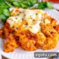 Close-up of a serving of Bubble Up Lasagna on a white plate, showcasing the rich meat sauce, melted cheese, and golden-brown biscuits, ready to be enjoyed.