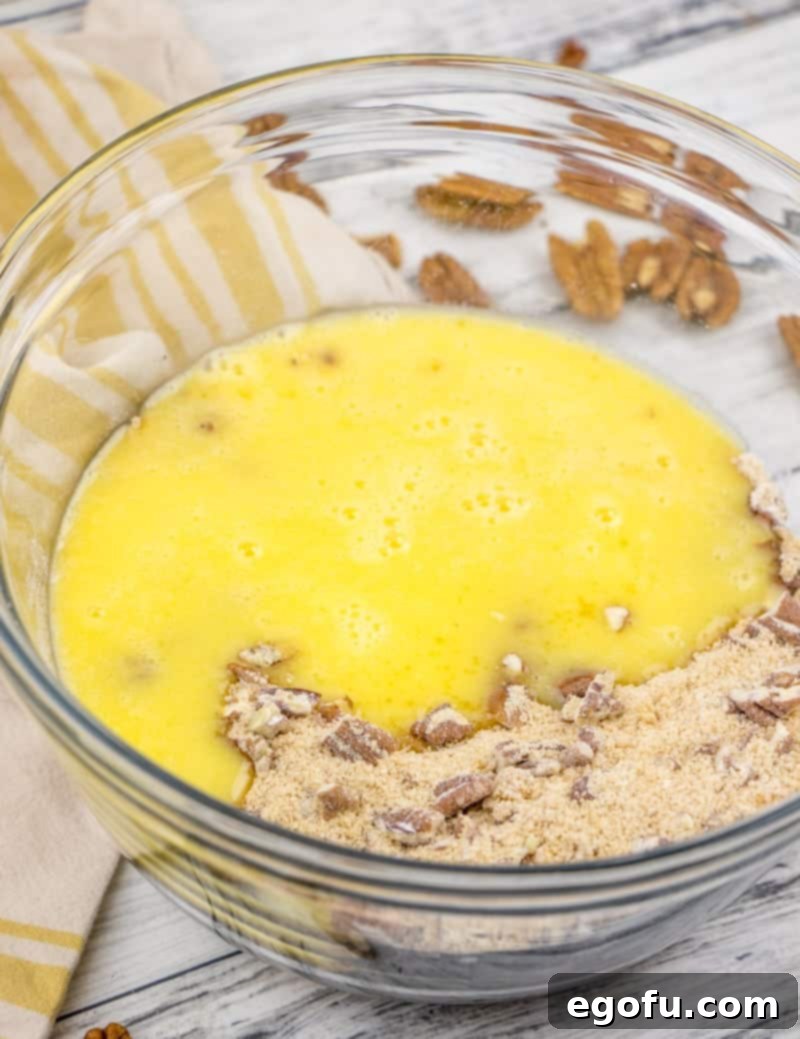 egg and melted butter being mixed with flour, brown sugar and chopped pecans in a bowl.