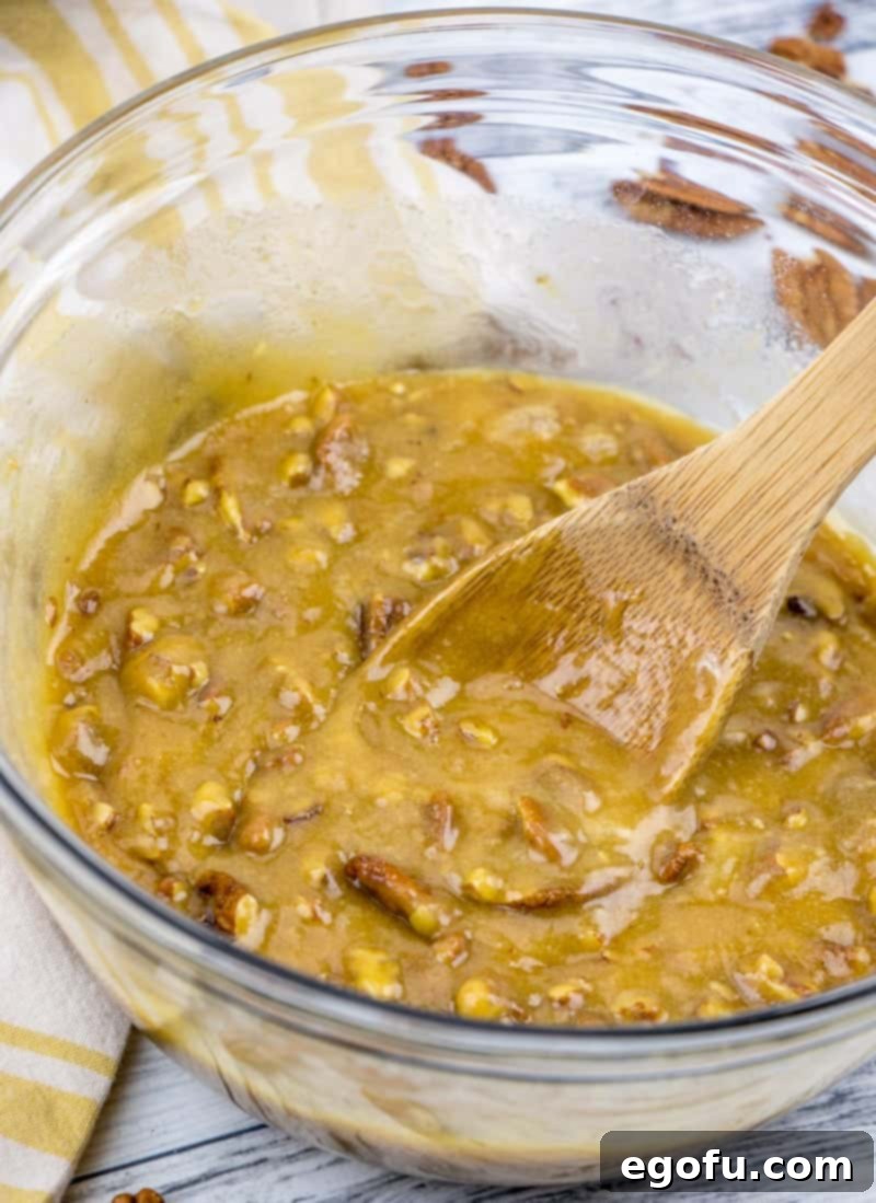 pecan pie muffin batter in a clear bowl being stirred with a wooden spoon.