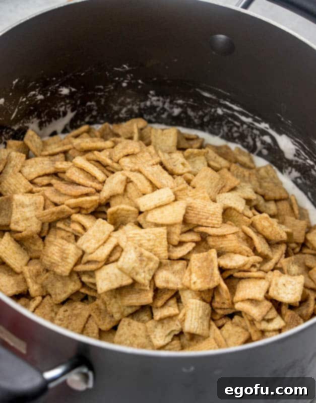 Cinnamon Toast Crunch cereal added to marshmallow butter mixture, being stirred