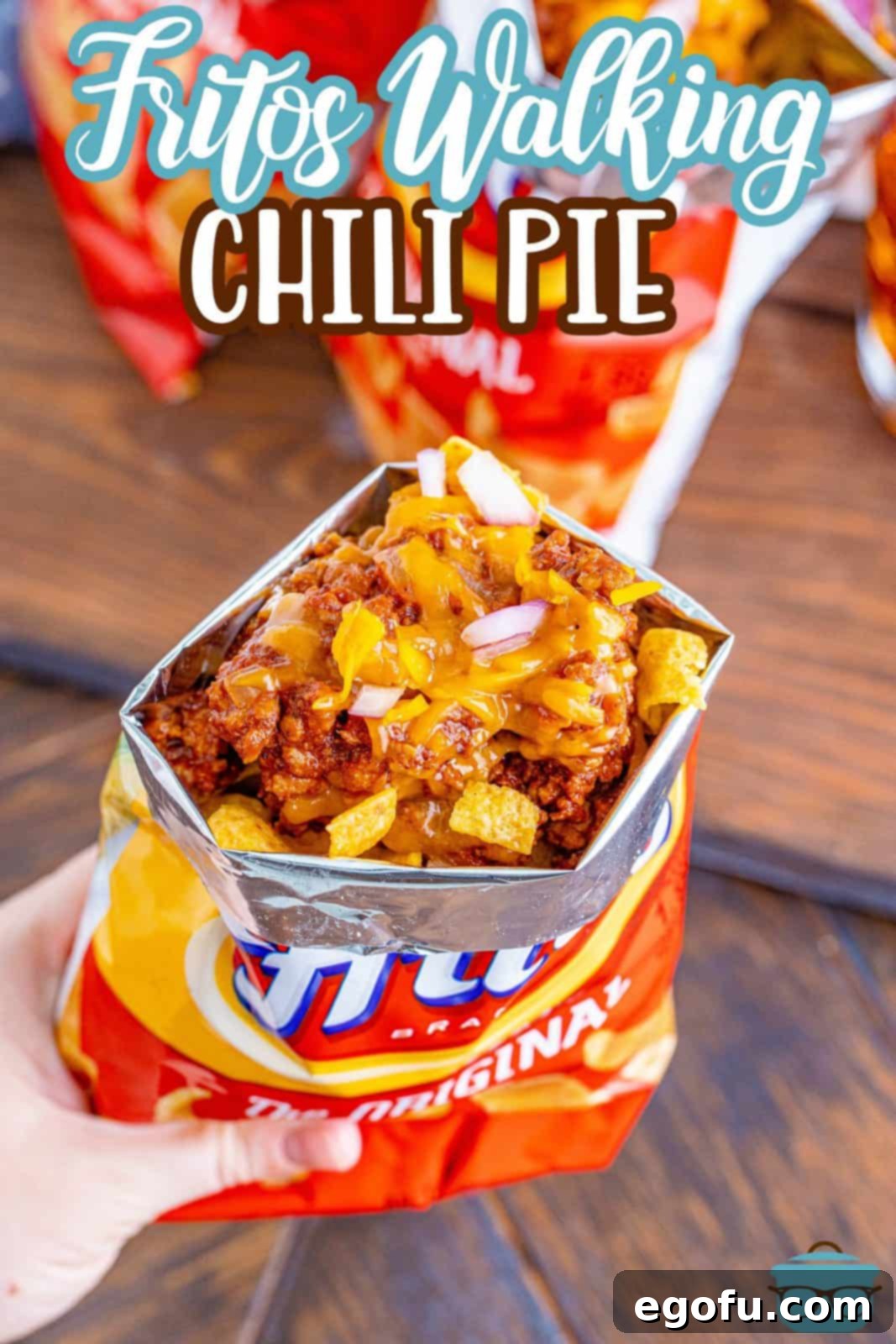 a hand holding a bag of Fritos corn chips that is topped with chili, cheese and diced onions.