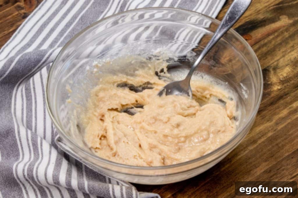 Melted butter and apple cinnamon muffin mix combined in a clear mixing bowl, forming a thick batter for the cobbler topping.