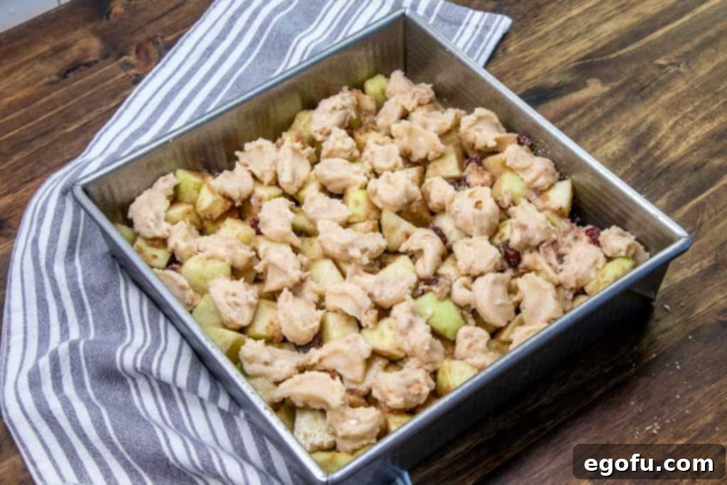 Apple cinnamon muffin mix batter dotted over the diced apple mixture in a baking dish, before baking.