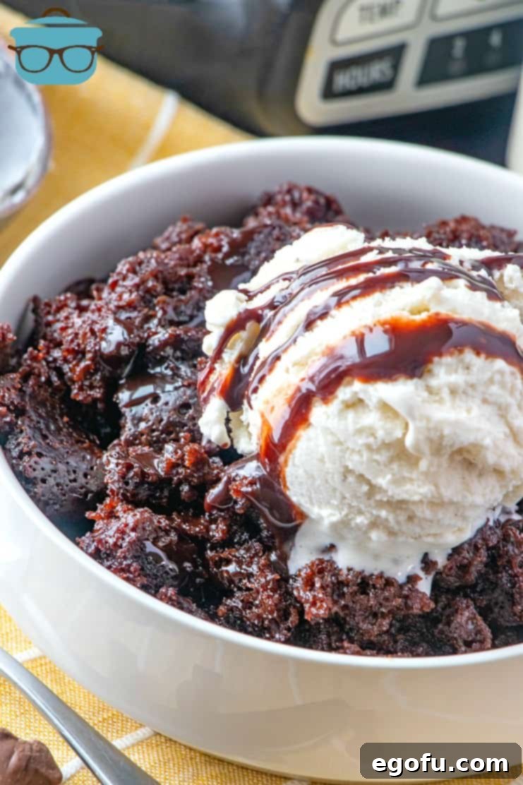 Decadent Slow Cooker Chocolate Pudding Cake 2 A serving of Slow Cooker Chocolate Fudge Cake in a white bowl, topped with a generous scoop of vanilla ice cream and drizzled with luscious chocolate sauce.