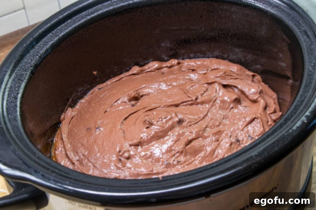 Decadent Slow Cooker Chocolate Pudding Cake 6 Chocolate cake batter smoothly spread at the bottom of a small oval slow cooker, ready for cooking.