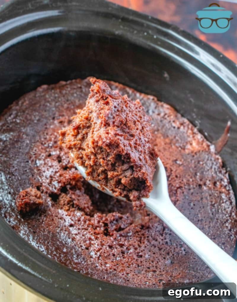 Decadent Slow Cooker Chocolate Pudding Cake 7 A close-up shot of the finished Crock Pot Chocolate Spoon Cake, ready to be served, with a white spoon gently scooping a portion of the moist, dark chocolate cake.