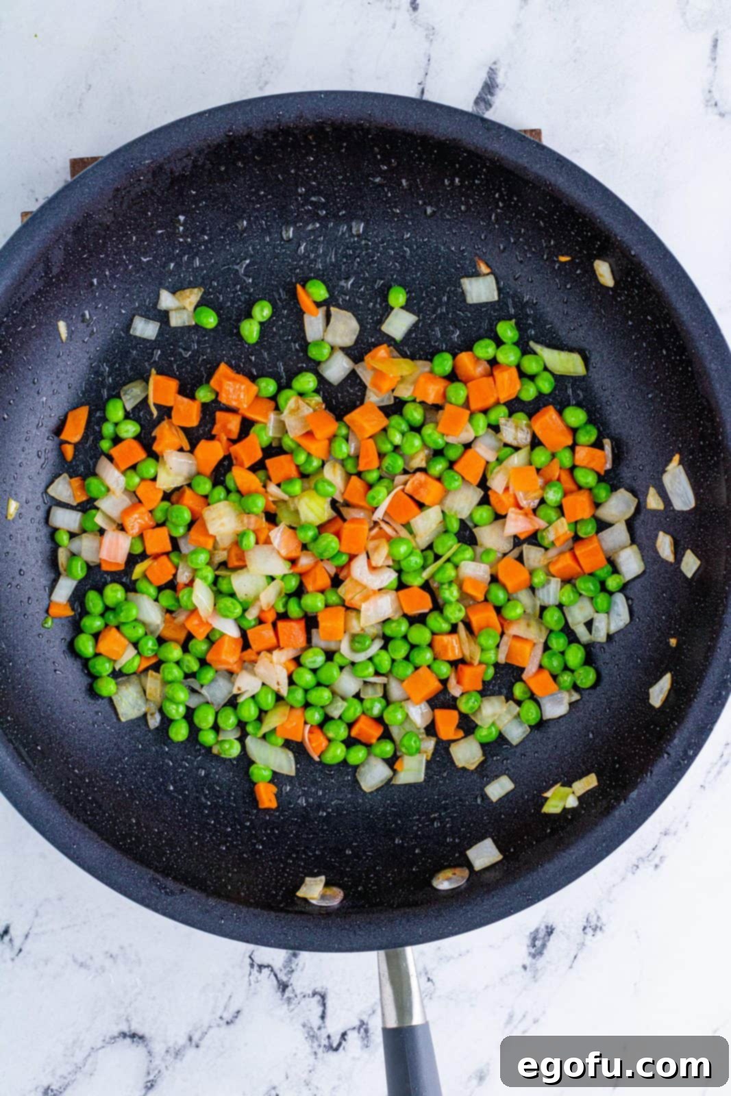 Sizzling Beef Fried Rice 6 Onions, peas and carrots cooking in pan.
