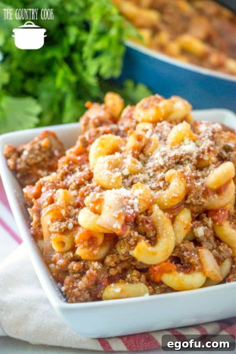 A square white bowl brimming with hearty American Goulash, garnished with fresh parsley, ready to be served.