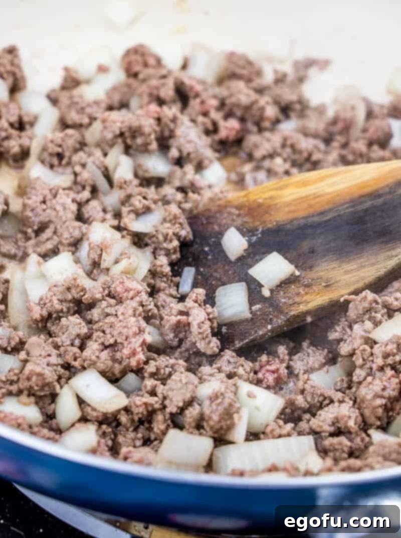 Browned and crumbled ground beef mixed with diced onions in a large skillet, cooking over medium heat.