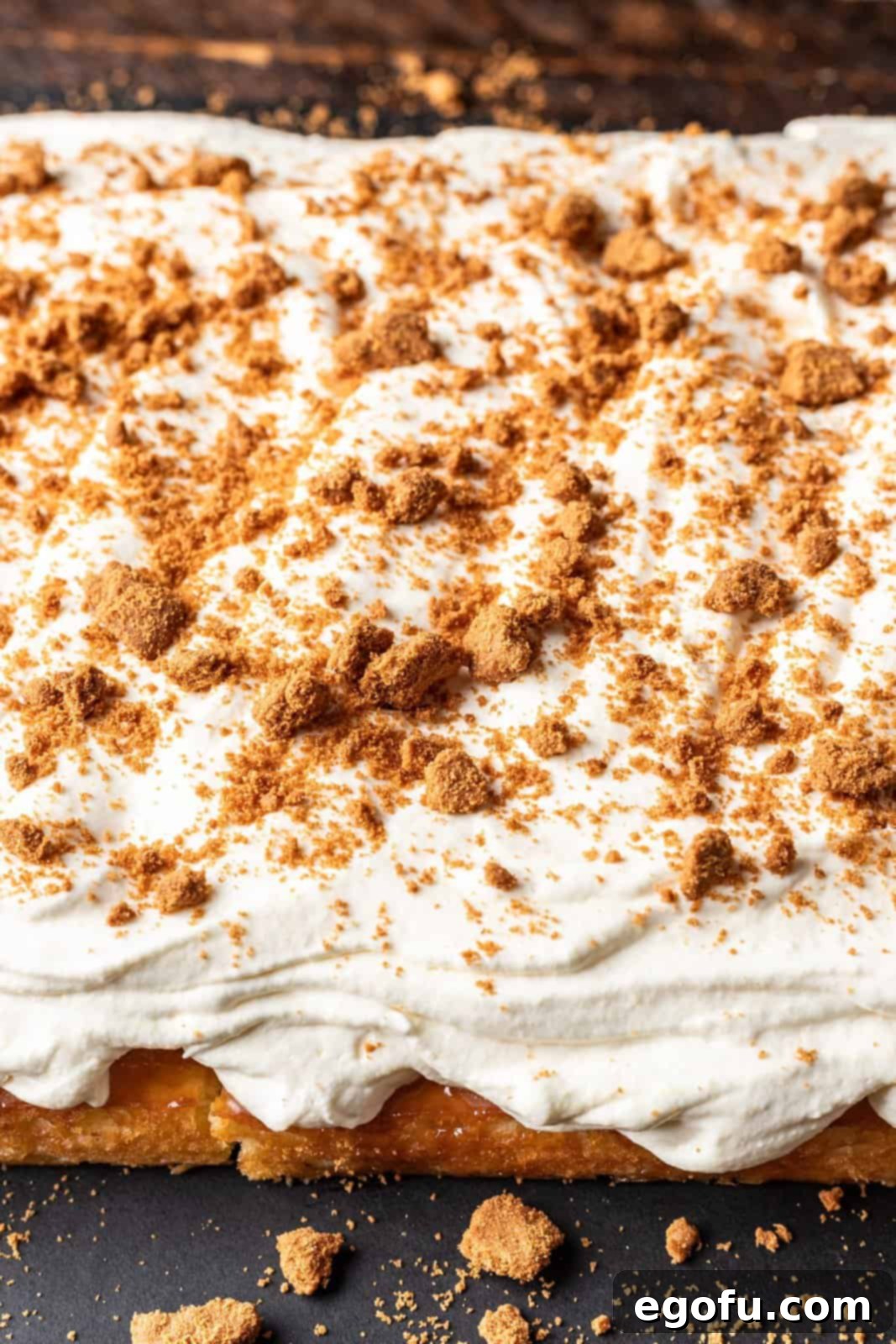 New Orleans Bananas Foster Poke Cake 10 Finely crushed Biscoff cookies being sprinkled evenly over the top of the Bananas Foster Poke Cake, adding a spiced, crunchy finish.