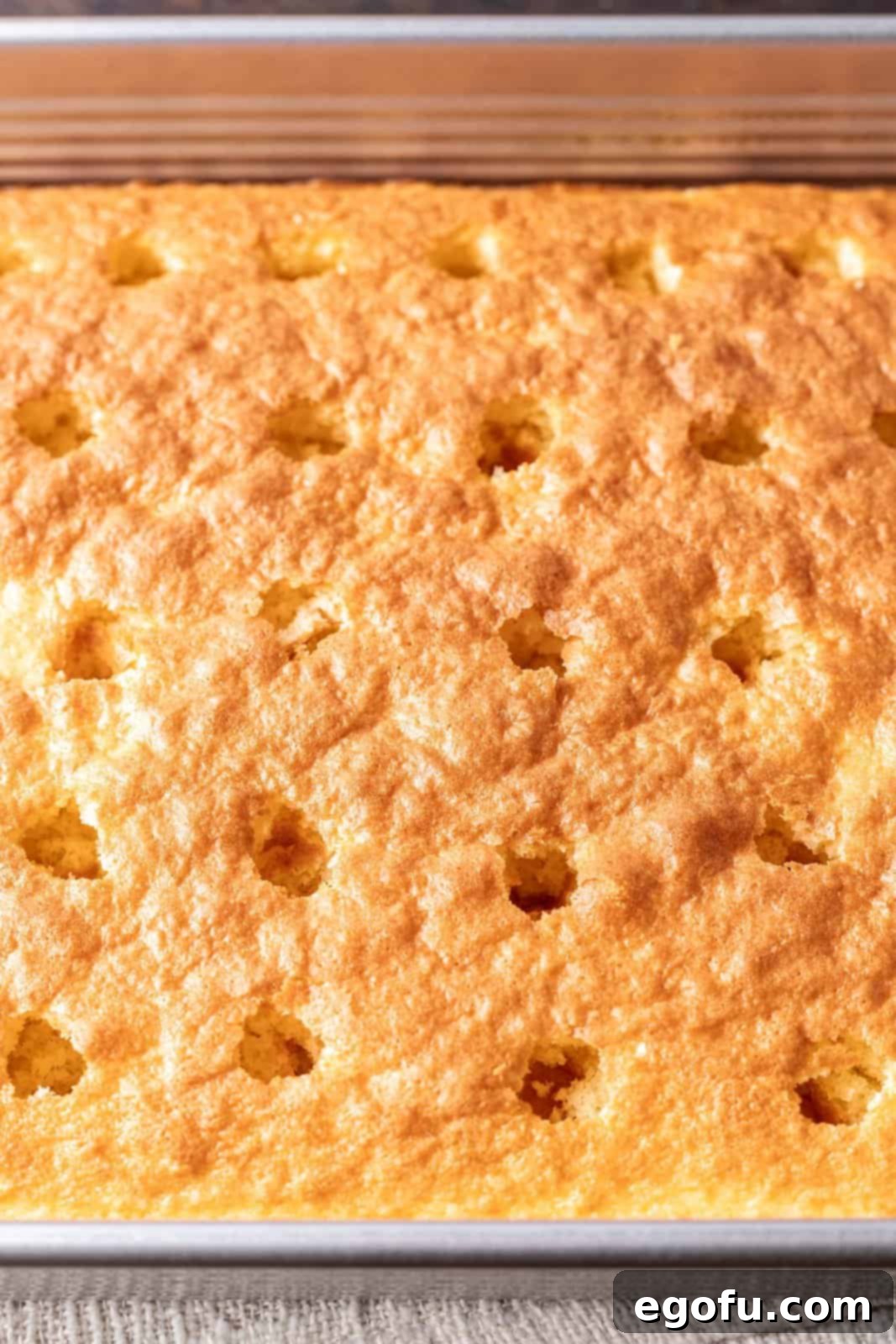 New Orleans Bananas Foster Poke Cake 4 A freshly baked cake in a 9x13-inch baking dish with large holes poked evenly across its surface, preparing for the caramel infusion.