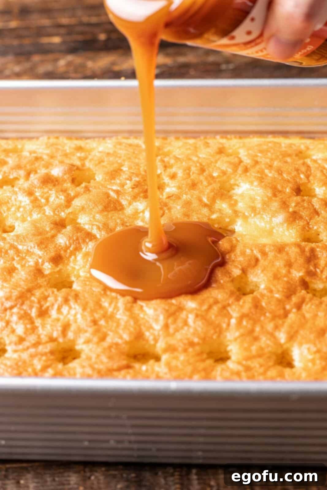 New Orleans Bananas Foster Poke Cake 5 Thick caramel sauce being carefully poured and spread into the poked holes of a warm cake, creating a rich, infused base.