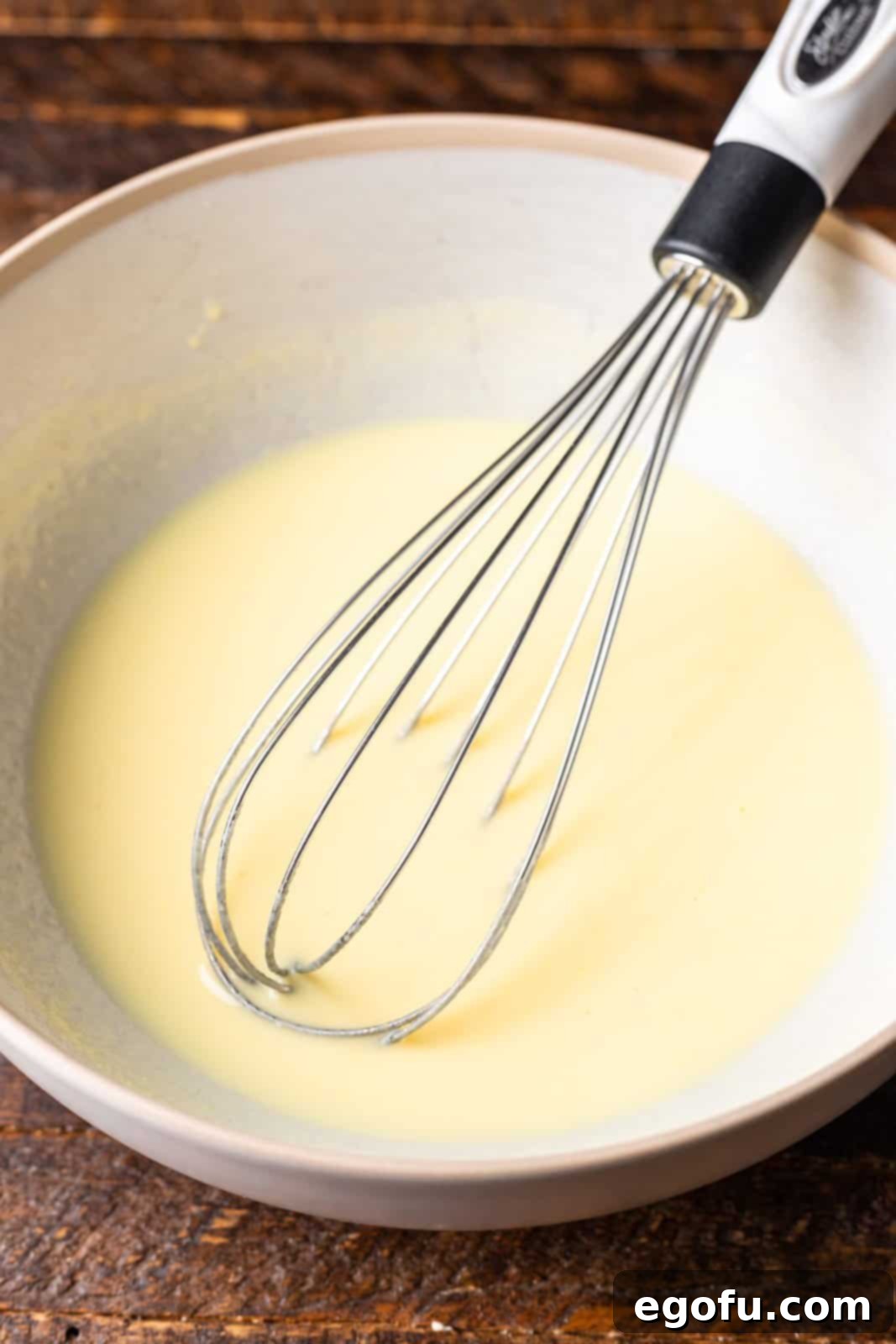 New Orleans Bananas Foster Poke Cake 7 Instant banana cream pudding being whisked together with milk in a bowl until smooth and starting to thicken, forming a creamy base for the topping.