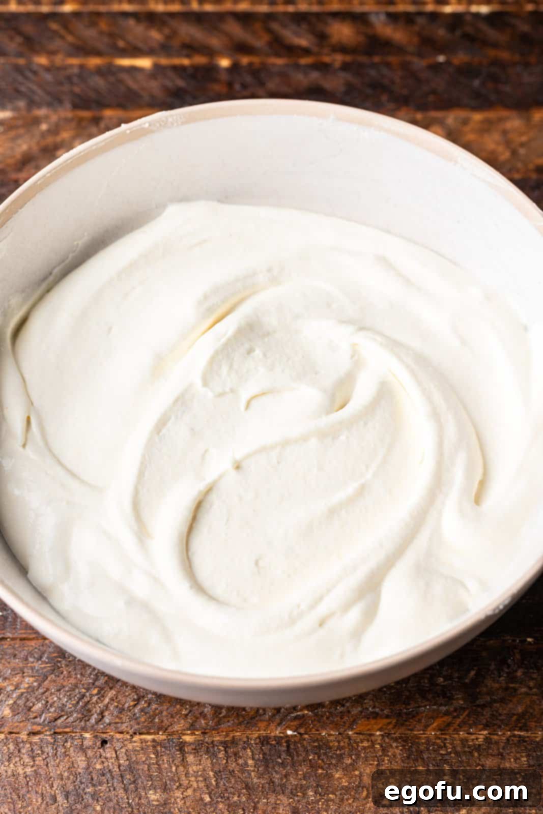 New Orleans Bananas Foster Poke Cake 8 Thawed Cool Whip being gently folded into the banana pudding mixture in a white bowl, creating a light and airy cake topping.