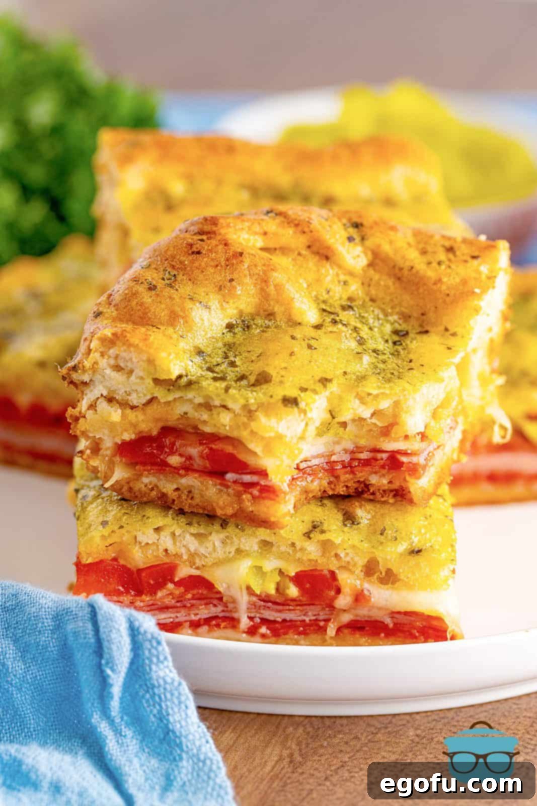 A stack of golden-brown Italian Sub Squares, with a bite taken out of the top one, revealing the delicious layers of meat and cheese.