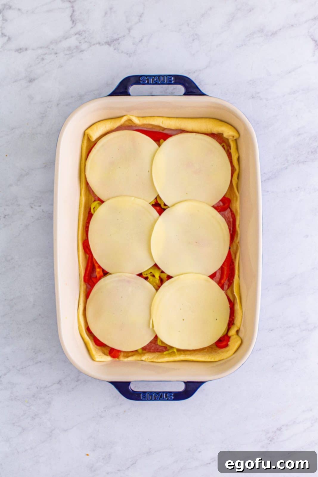 Layers of provolone cheese, pepperoni, ham, salami, roasted red bell peppers, and pepperoncini assembled in the baking dish.