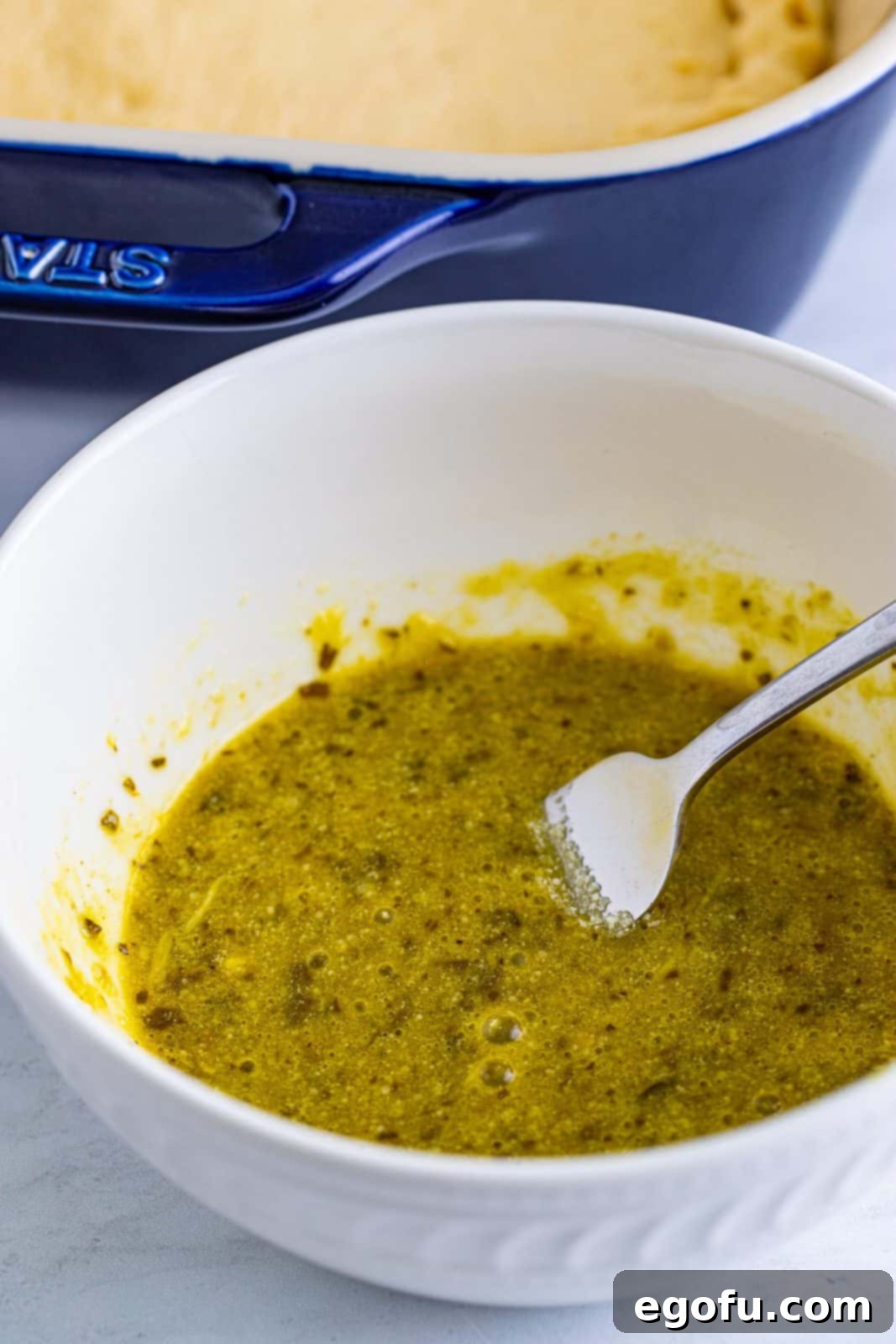 A small bowl containing whisked egg, pesto, and Parmesan cheese, ready to be brushed onto the dough.