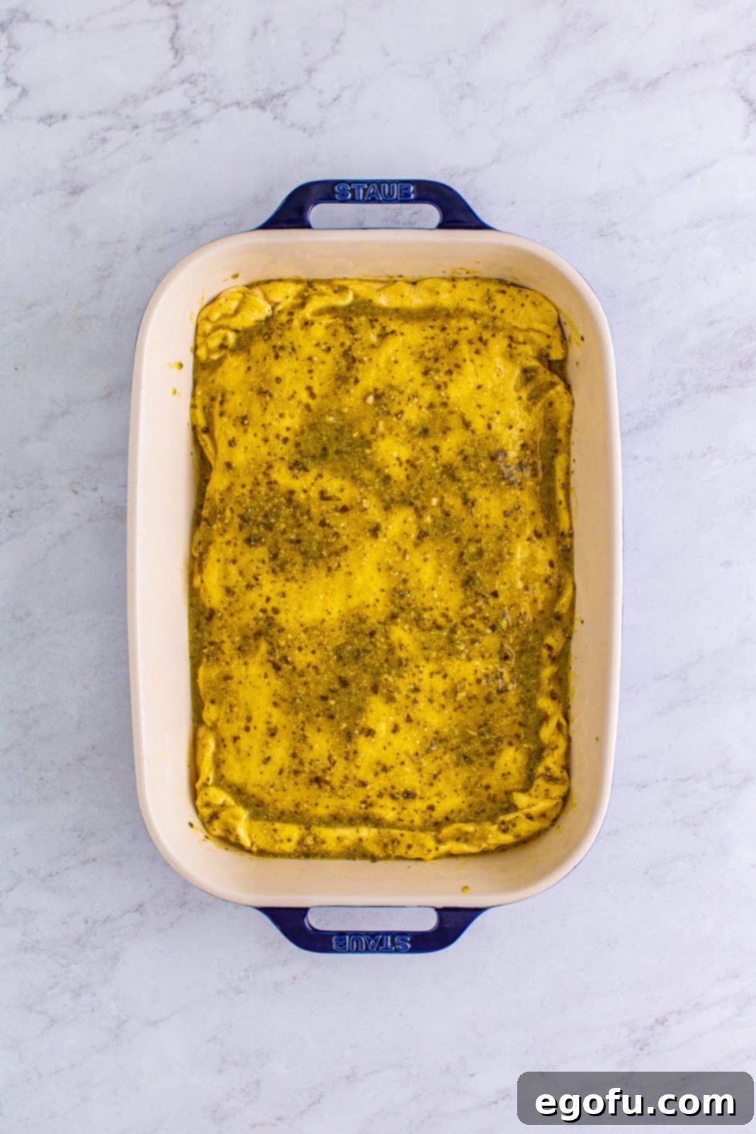 The pesto mixture expertly brushed across the top of the crescent dough sheet, ready for baking.