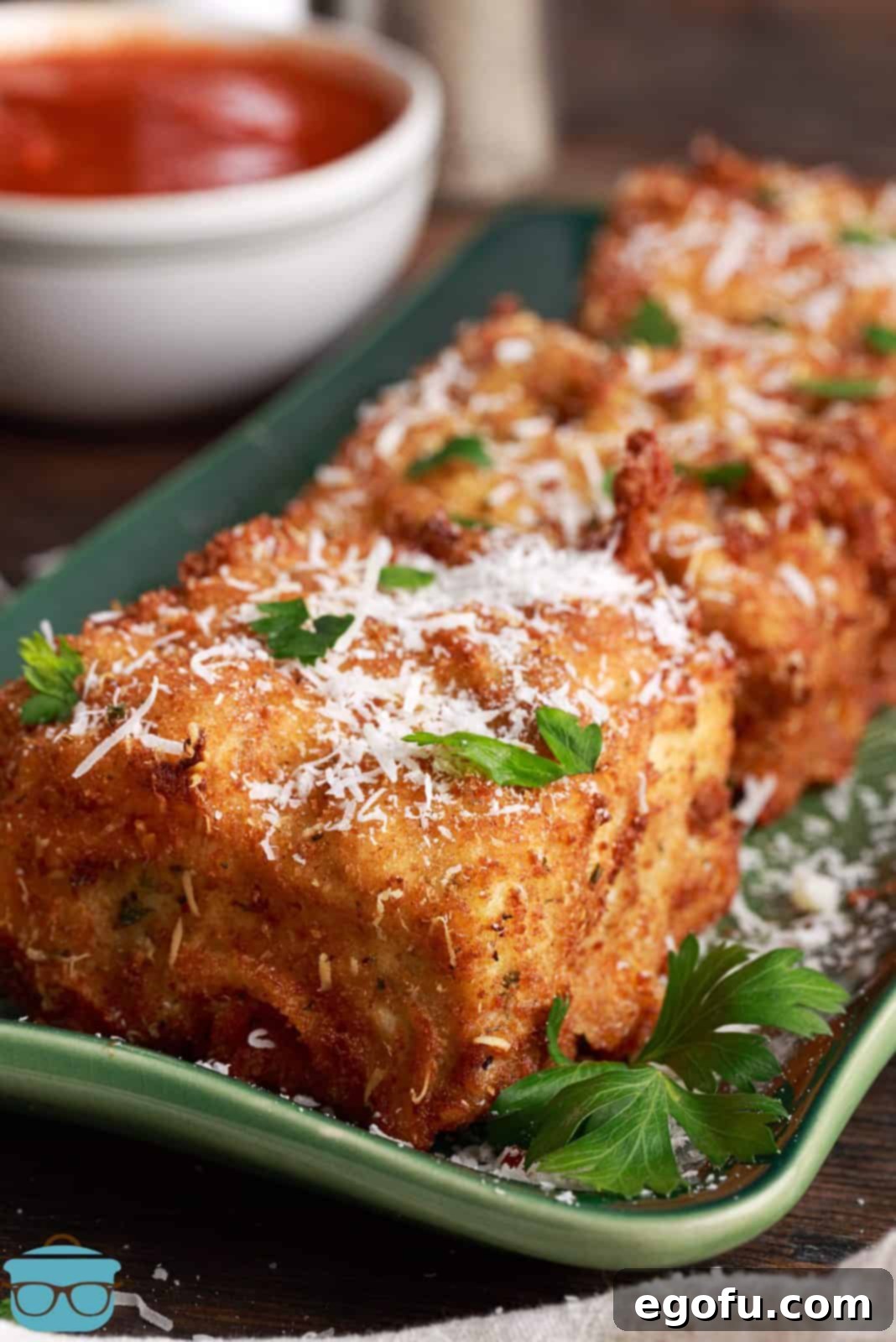 Finished Deep Fried Lasagna on green platter topped with shredded cheese and parsley, showcasing its golden crispy exterior and savory appeal.