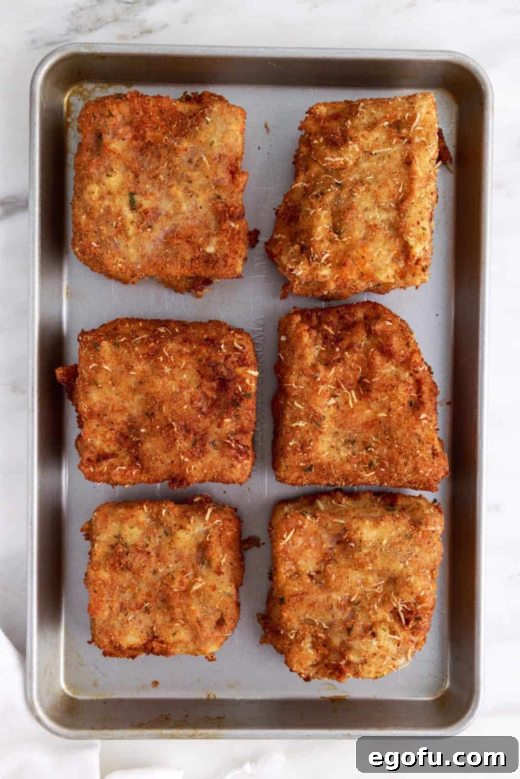 A baking sheet filled with perfectly golden-brown deep-fried lasagna pieces, ready to be served or finished in the oven.