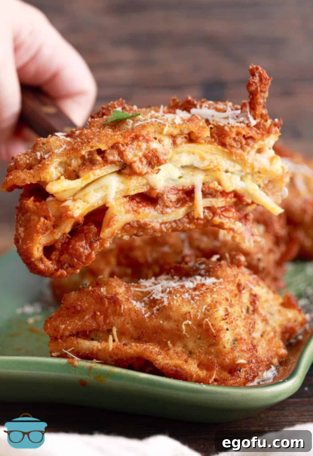 A spatula holding a piece of Deep Fried Lasagna cut in half, revealing the steaming, cheesy layers within its golden, crunchy crust.