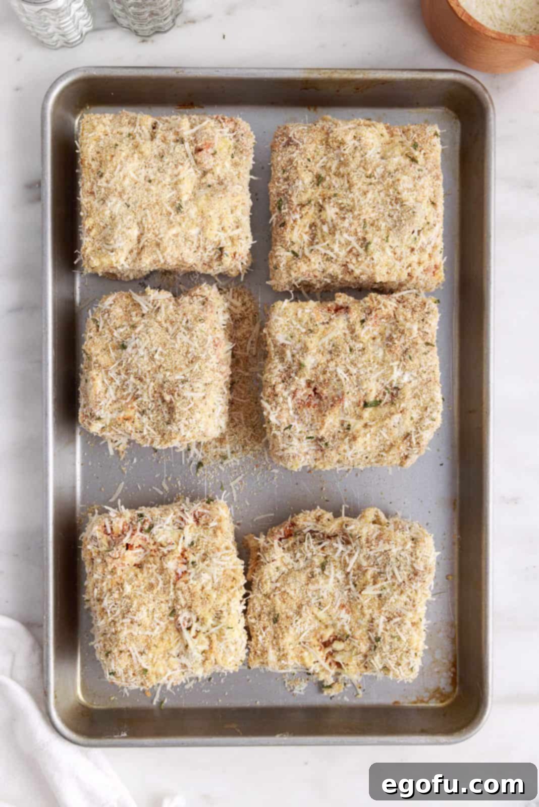 Several perfectly coated lasagna pieces neatly arranged on a sheet pan, ready for deep frying, showcasing the even breading.
