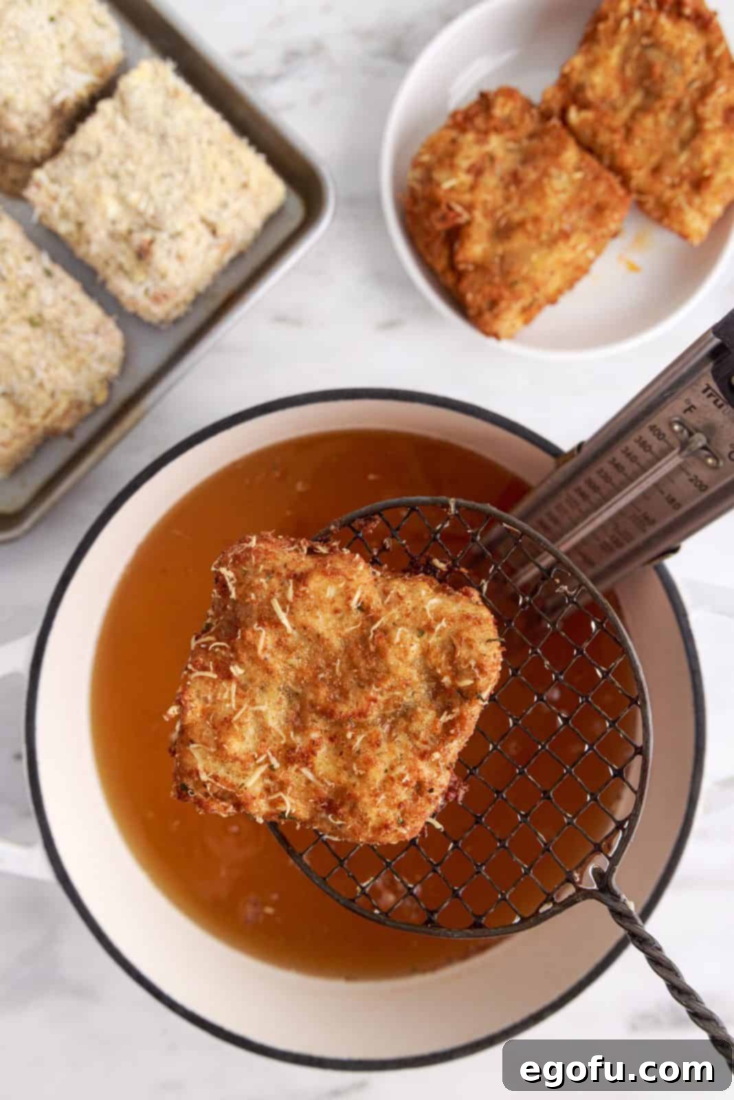 A spider strainer expertly lifting a golden-brown piece of deep-fried lasagna out of the hot oil, demonstrating the removal process.
