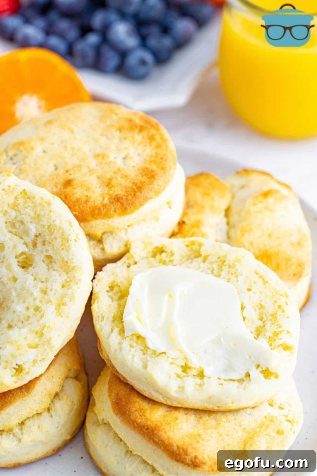 A freshly baked cream biscuit split open, with butter being spread on the inside.