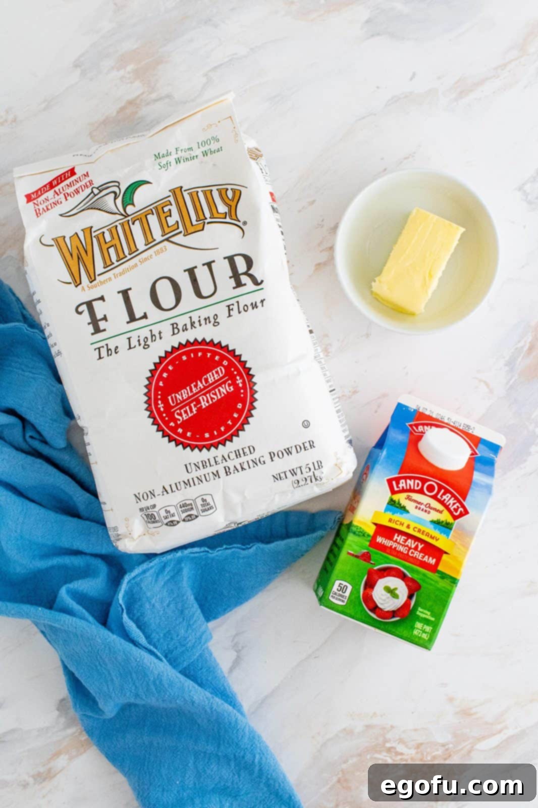 Key ingredients laid out: A bag of self-rising flour, a carton of heavy cream, and a stick of butter.