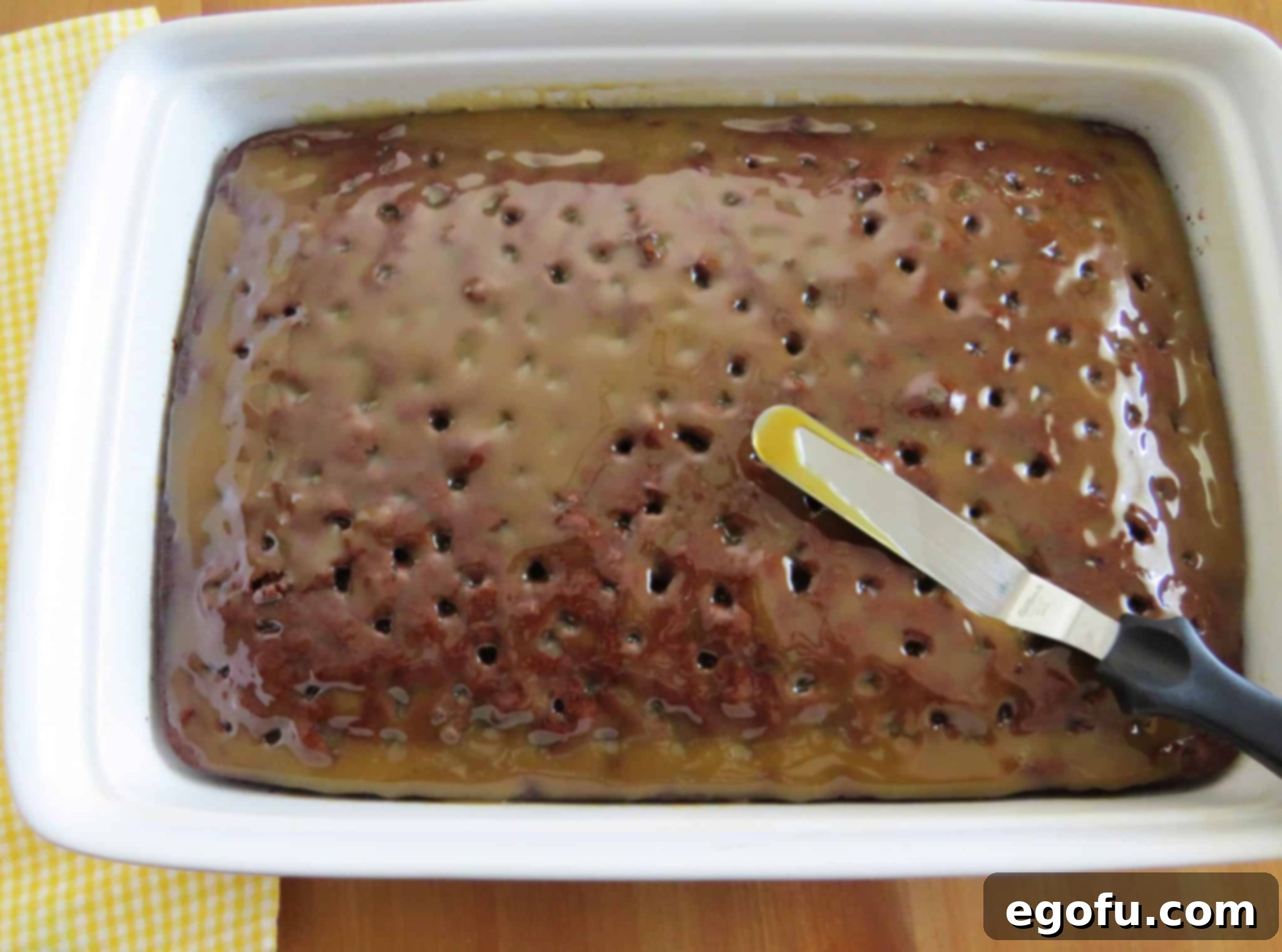 an offset spatula spreading out caramel sauce on chocolate cake.