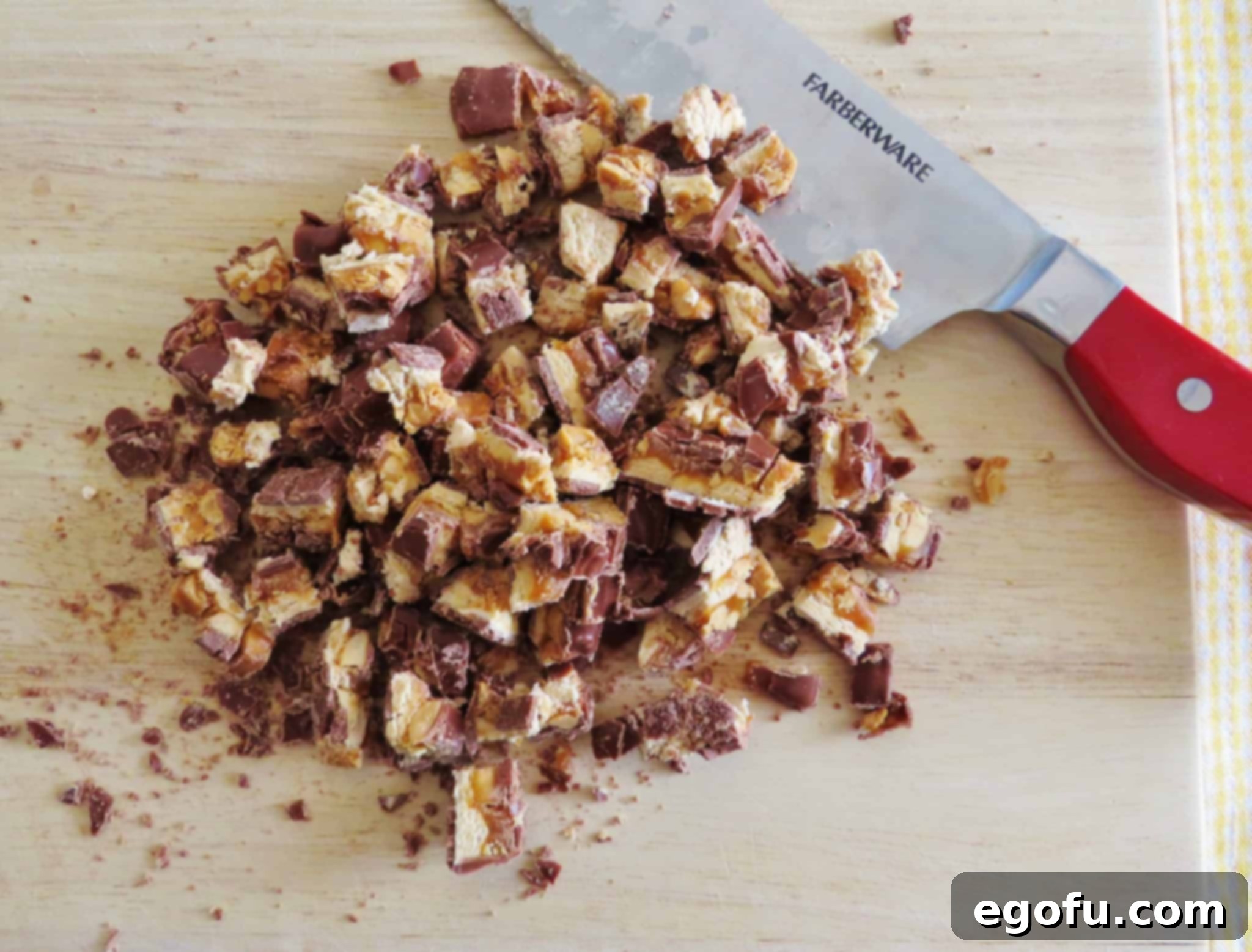 chopped Snickers candy bars on a wooden cutting board with a knife set to the side.