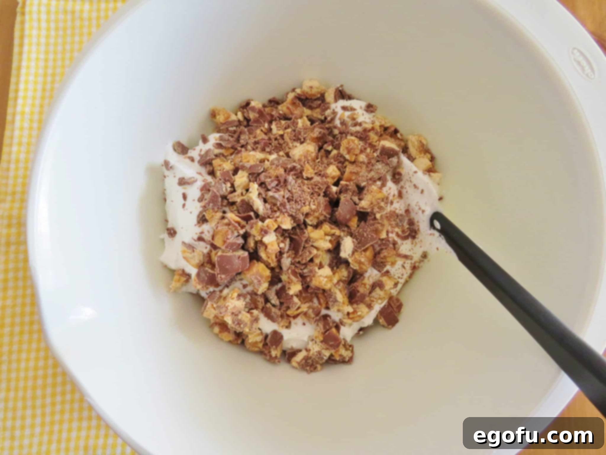 chopped snickers candy bars on top of whipped topping in a white mixing bowl.