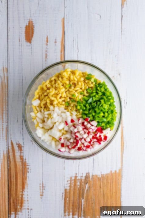 Macaroni, peppers, radishes, and onion in a mixing bowl.