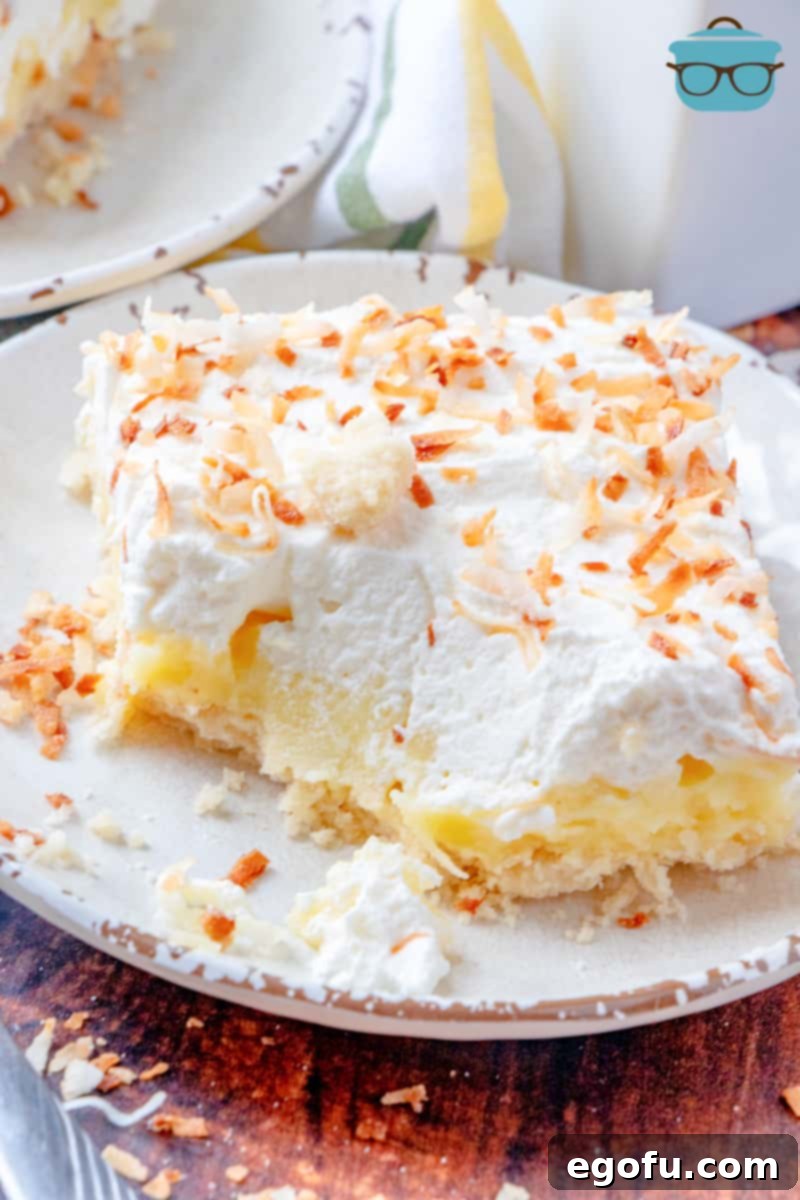 Slice of coconut cream bar on a white plate with a bite removed and sprinkled with toasted coconut, showcasing its alluring layers.