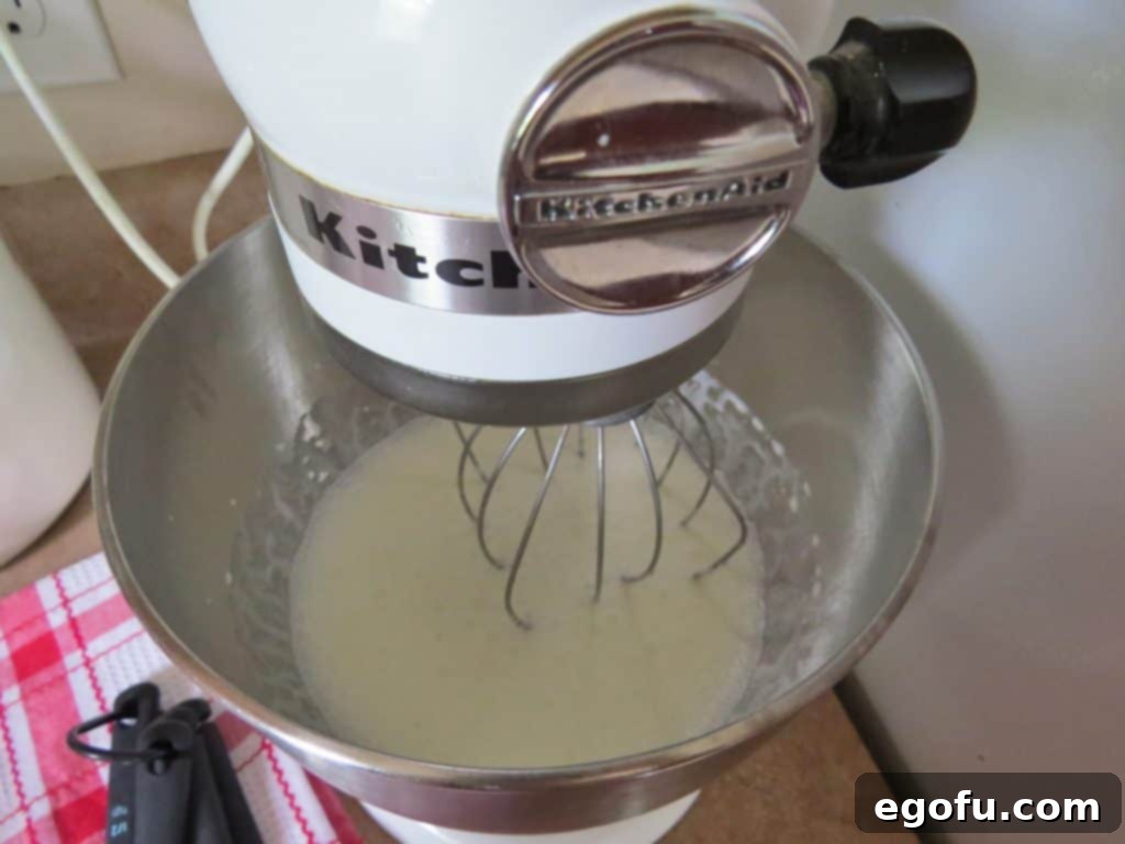 A stand mixer with a whisk attachment actively whipping very cold heavy cream, illustrating the process of preparing the fluffy topping for the dessert bars.