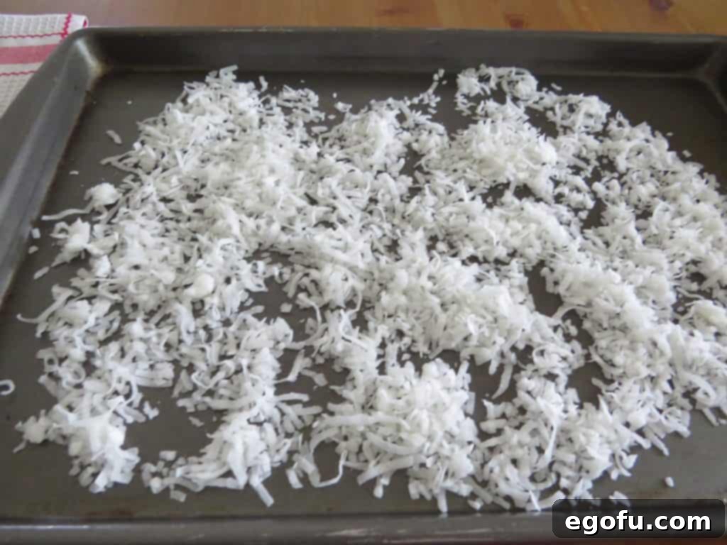Sweetened shredded coconut spread thinly and evenly onto a clean cookie sheet, meticulously arranged and ready to be toasted to perfection in the oven.