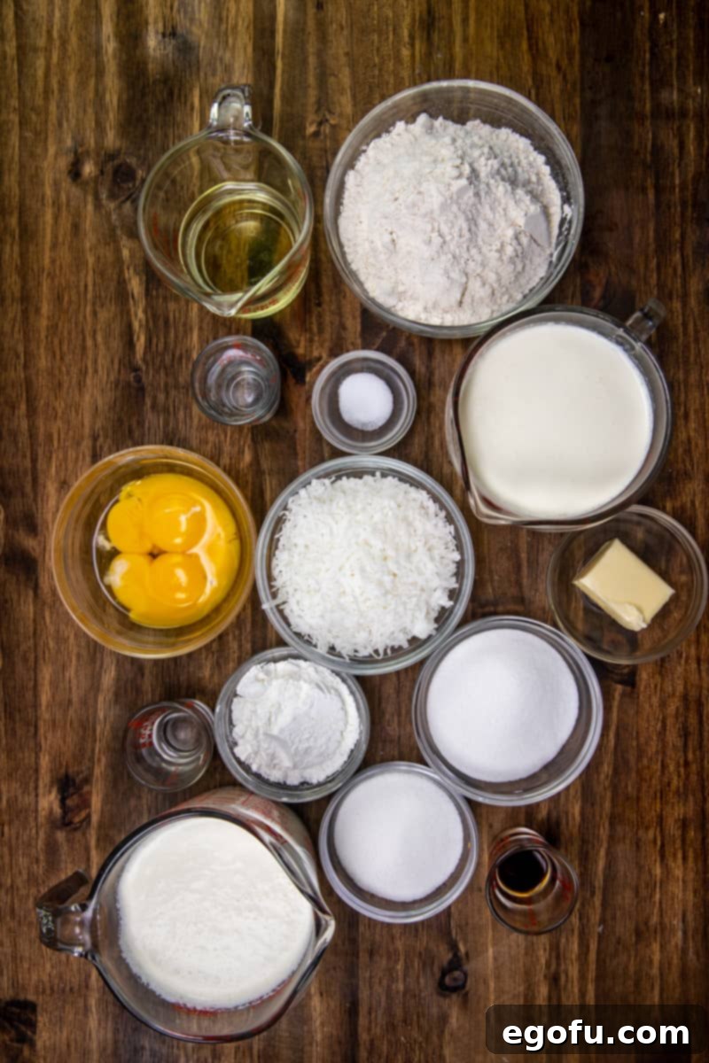 A comprehensive flat lay photograph showcasing all the ingredients required for coconut cream pie bars, meticulously arranged, including flour, salt, oil, water, sugar, cornstarch, half and half, egg yolks, butter, sweetened flaked coconut, coconut extract, heavy whipping cream, and powdered sugar, ready for preparation.