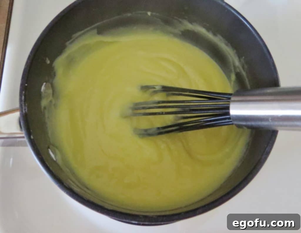 Close-up shot of the thickened, creamy coconut cream filling in a black saucepan, with a whisk demonstrating its rich, velvety texture after being cooked.